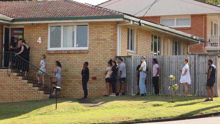 An old brick house with people lined up across the yard, up the stairs and into the house as though they're waiting to inspect it.